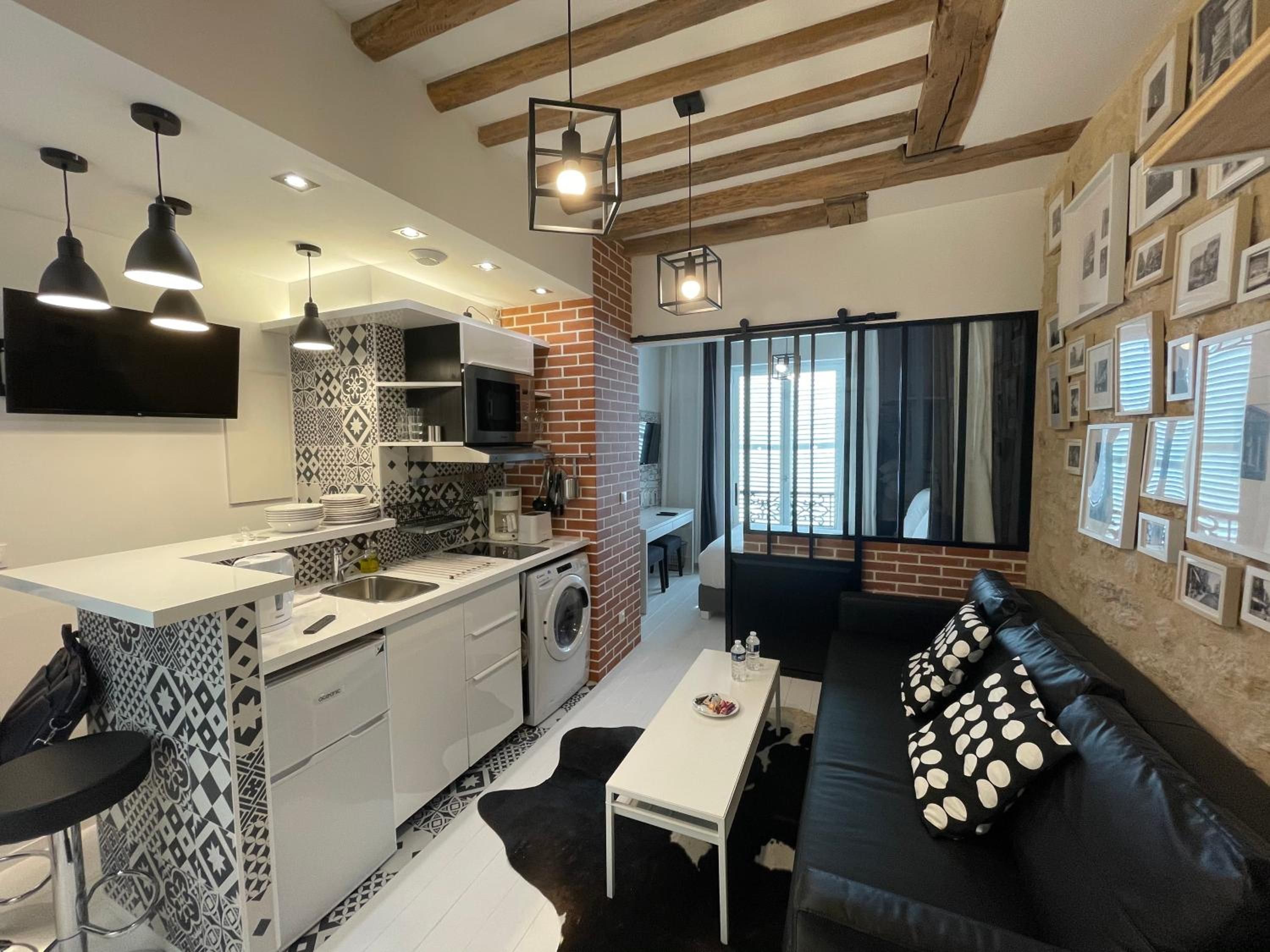 A modern kitchen with a built-in microwave, a coffee machine, and a washing machine. There is a black sofa with white polka dot cushions and a white coffee table.