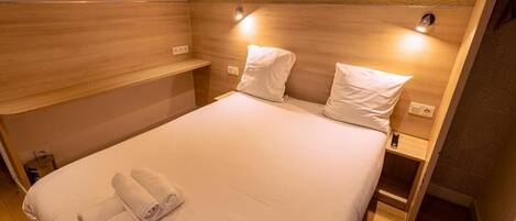 A hotel room with a bed, two bedside tables, and a headboard with built-in lighting.