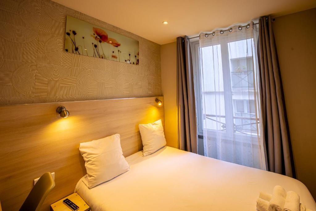 A hotel room with a bed, a headboard, a wall-mounted artwork, a window with curtains, and a bedside table with a lamp.