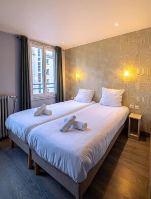 A hotel room with a double bed, two bedside tables, a window with curtains, and a patterned wall. - Hôtel Aix Europe (Paris)