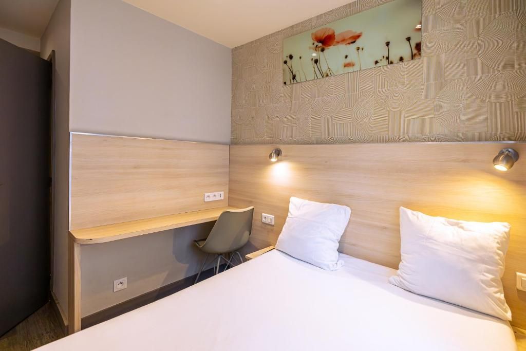 A hotel room with a bed, a desk, a chair, and a wall-mounted artwork.