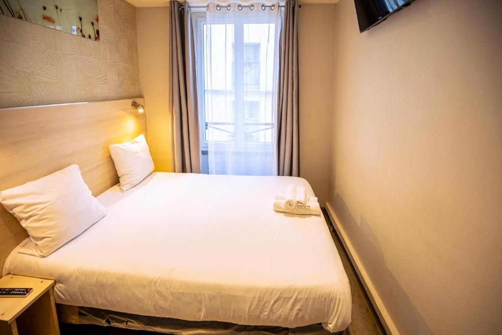 A hotel room with a bed, a nightstand, a TV mounted on the wall, and a window with curtains.