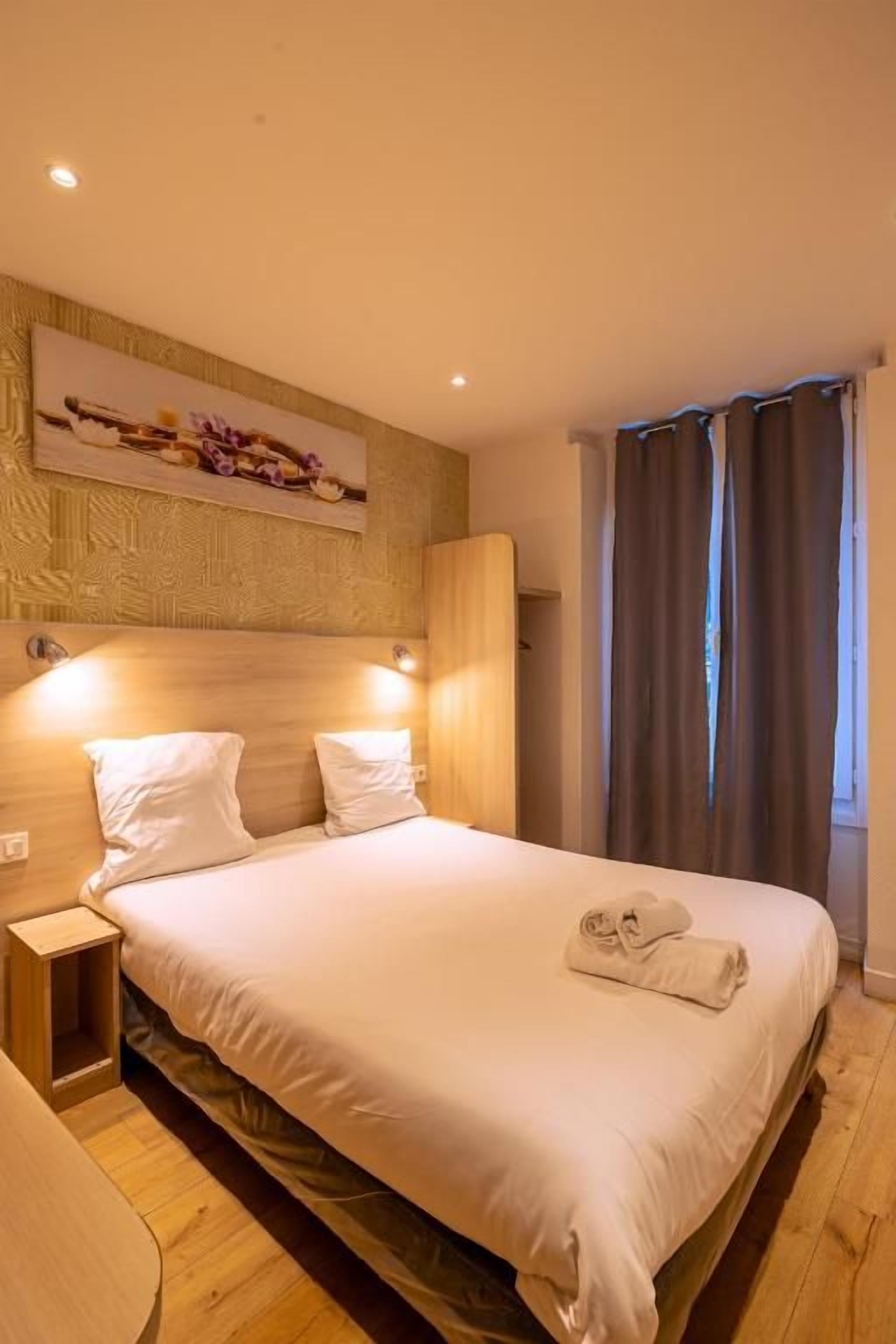 Ein Hotelzimmer mit Bett, Nachttischen, Kopfteil und einem an der Wand hängenden Kunstwerk.