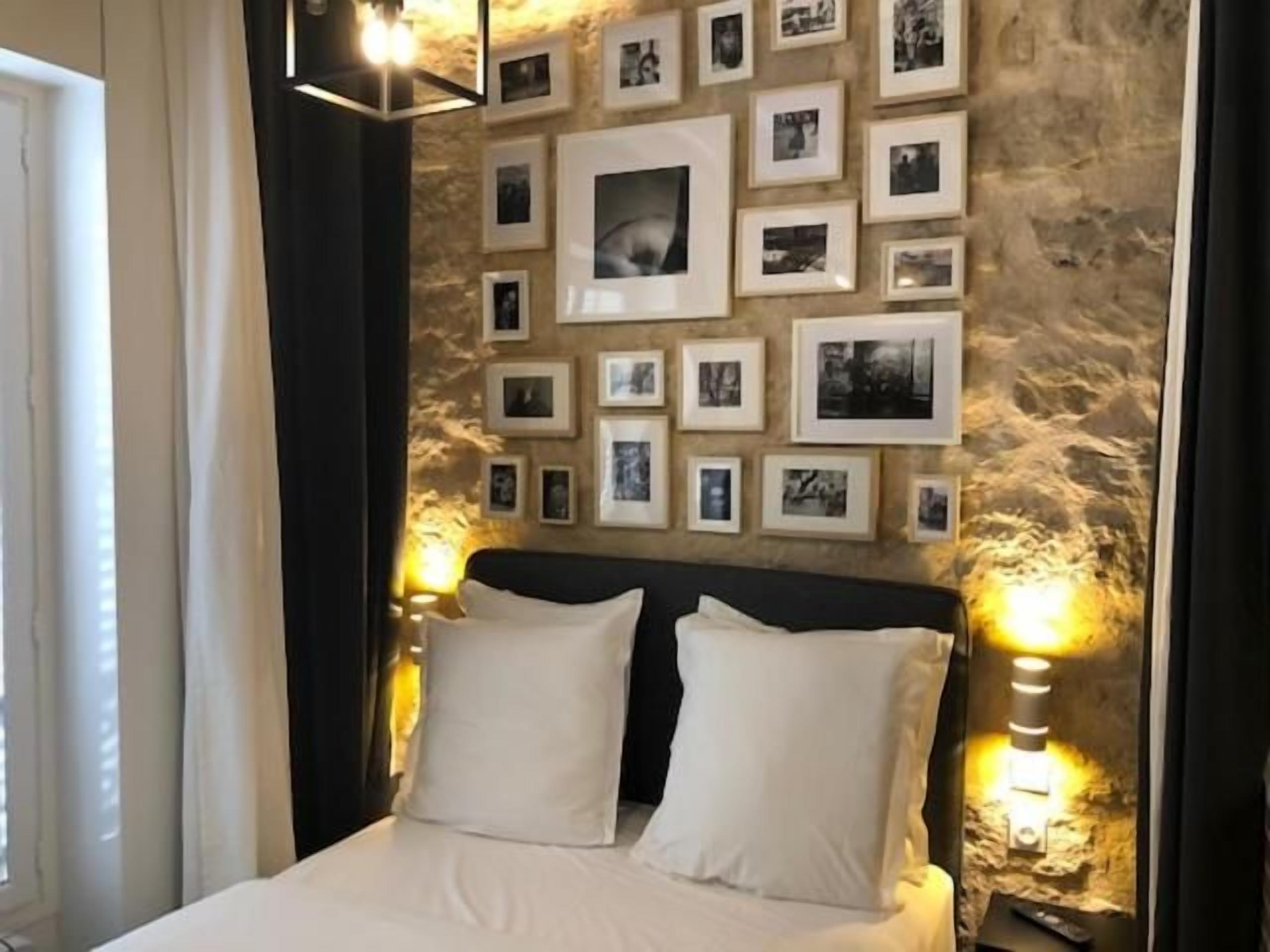 Un dormitorio con una cama, cuadros en la pared y dos lámparas de pared.