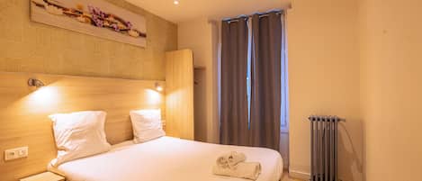 A neatly made bed with white linens, a wooden headboard, and a small bedside table with a lamp.