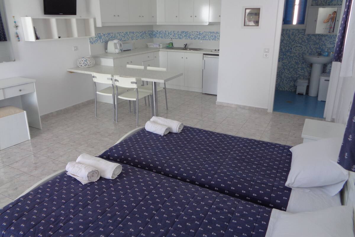 A compact hotel room with two beds, a small kitchenette, a dining area, and a bathroom.