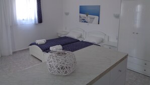 A bedroom with two beds, a bedside table, a wardrobe, a hanging light fixture, and a painting on the wall. - Blue and White Studios & Apartments (Karpathos)