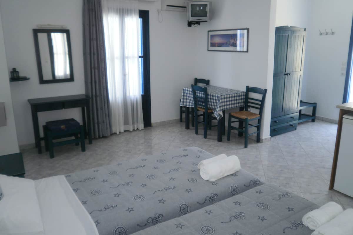 A hotel room with a bed, a desk, a chair, a table with a checkered tablecloth, a television, a picture on the wall, and a window with curtains.