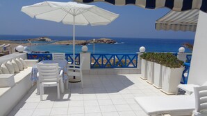 A terrace with white furniture, a white umbrella, and a view of the sea. - Blue and White Studios & Apartments (Karpathos)