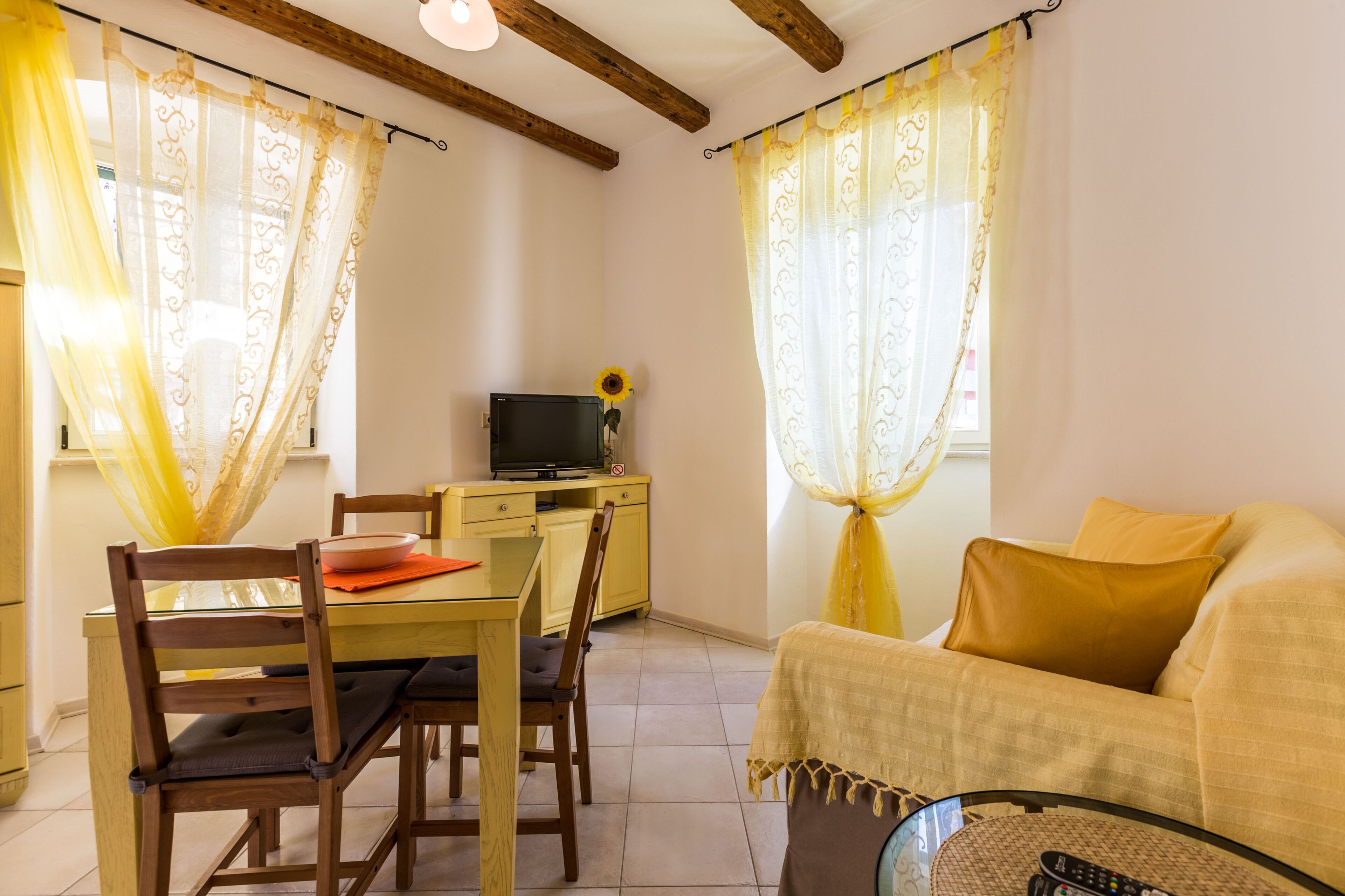 A cozy room with a dining table, chairs, a sofa, a TV, and curtains.