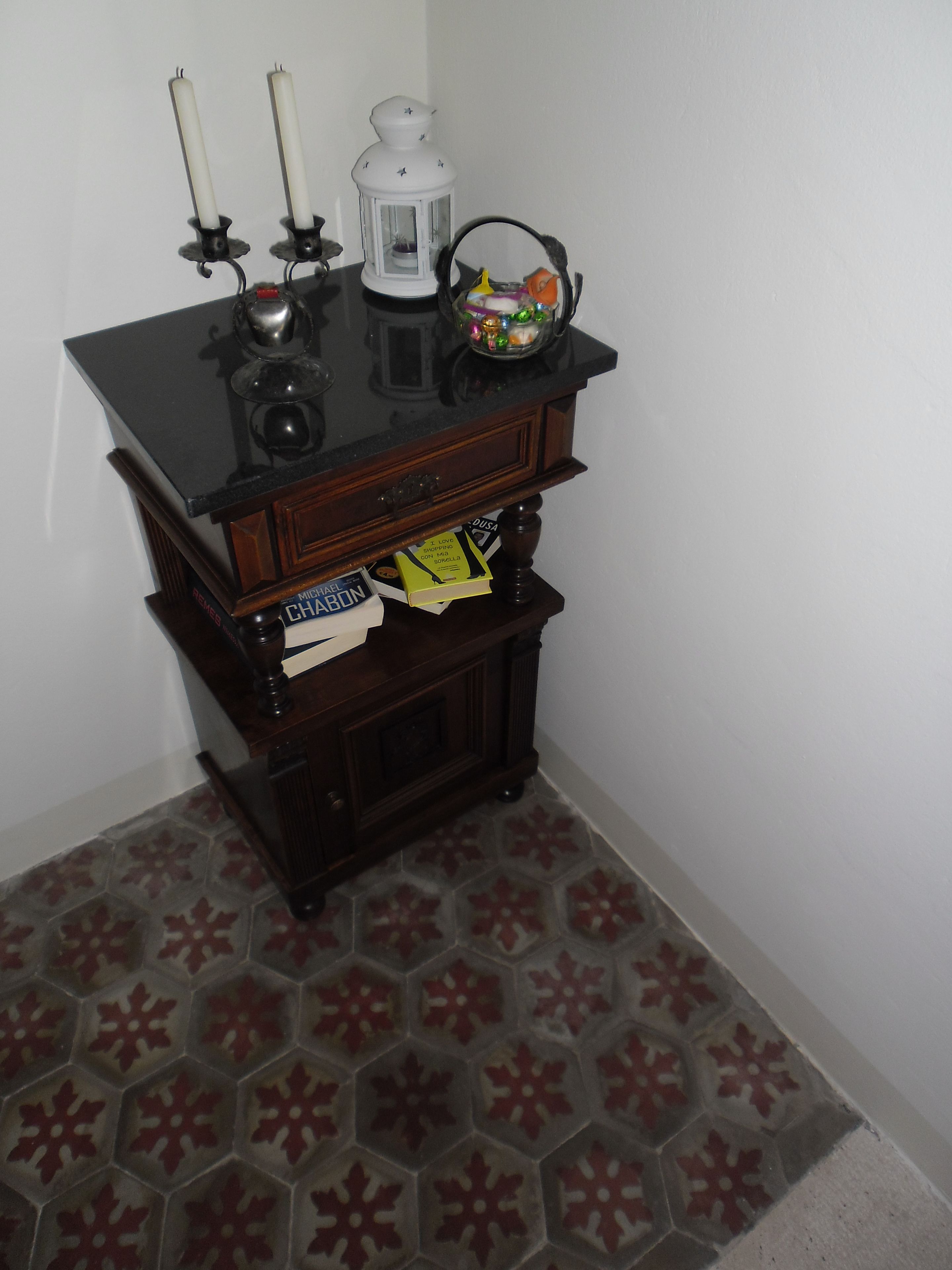 A corner with a dark wooden cabinet, a white wall, and a patterned floor.