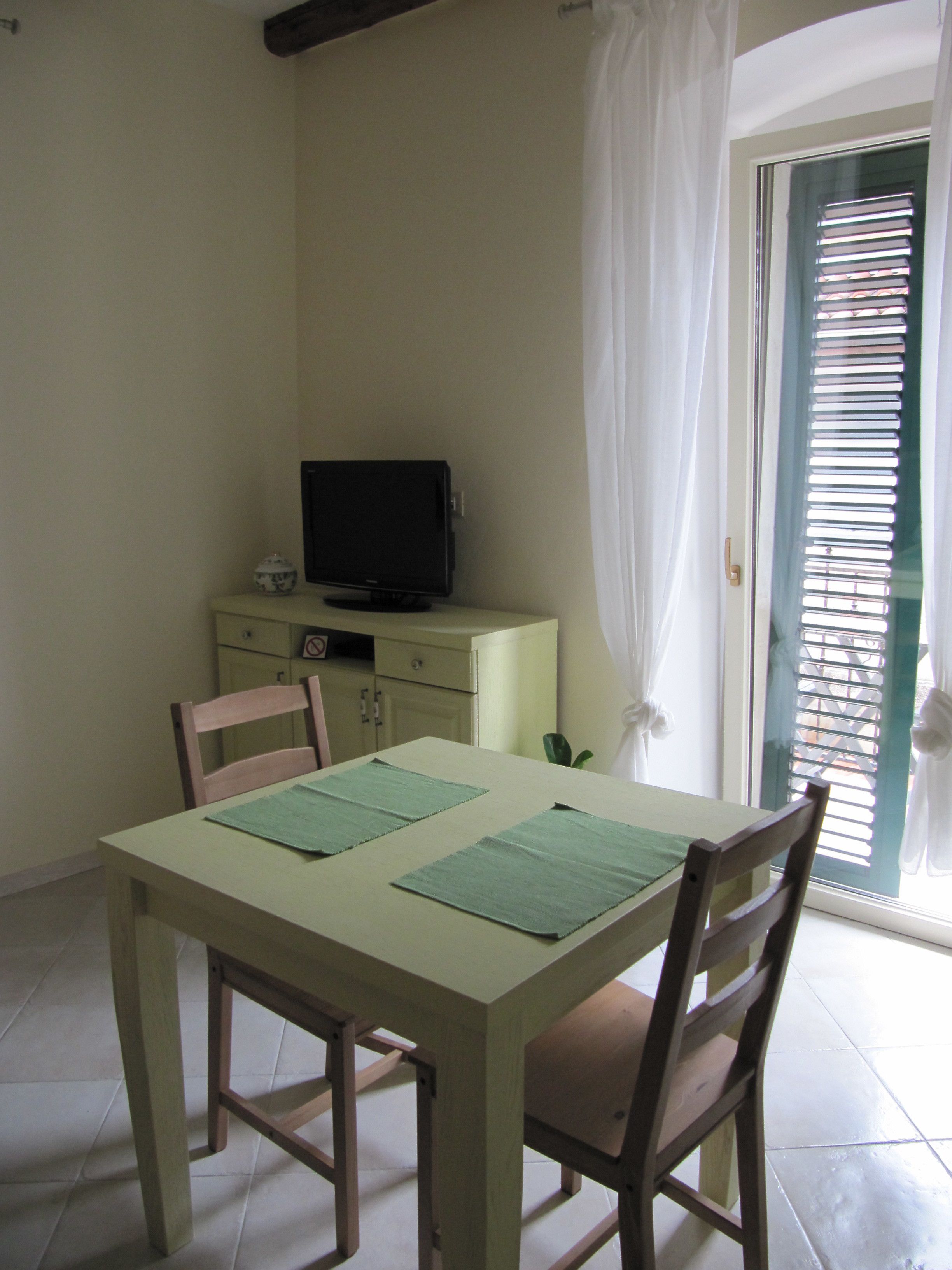 A dining area with a table, chairs, a television on a cabinet, and a window with blinds.