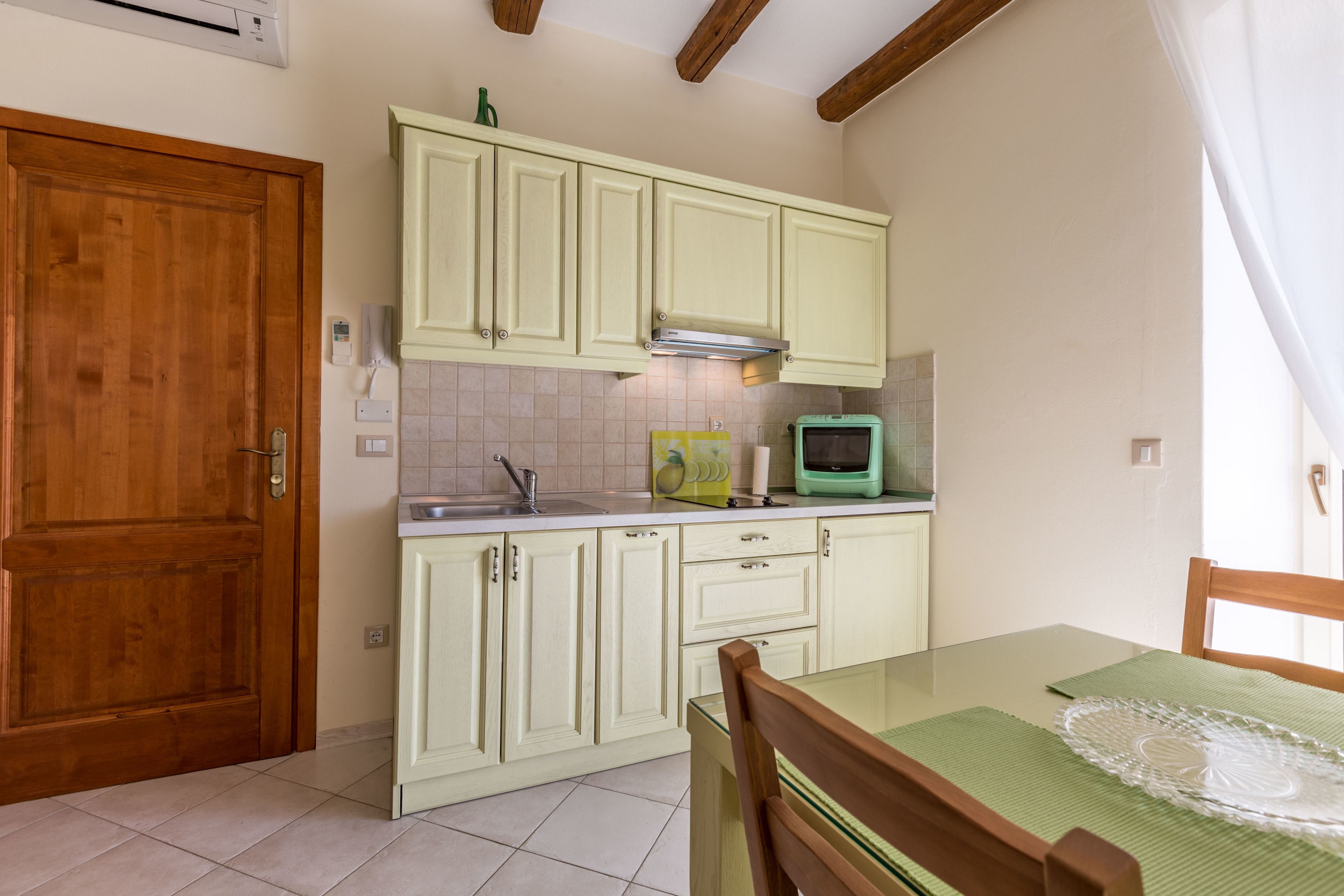 A kitchen with light green cabinets, a wooden door, a green television, and a table with a green placemat.