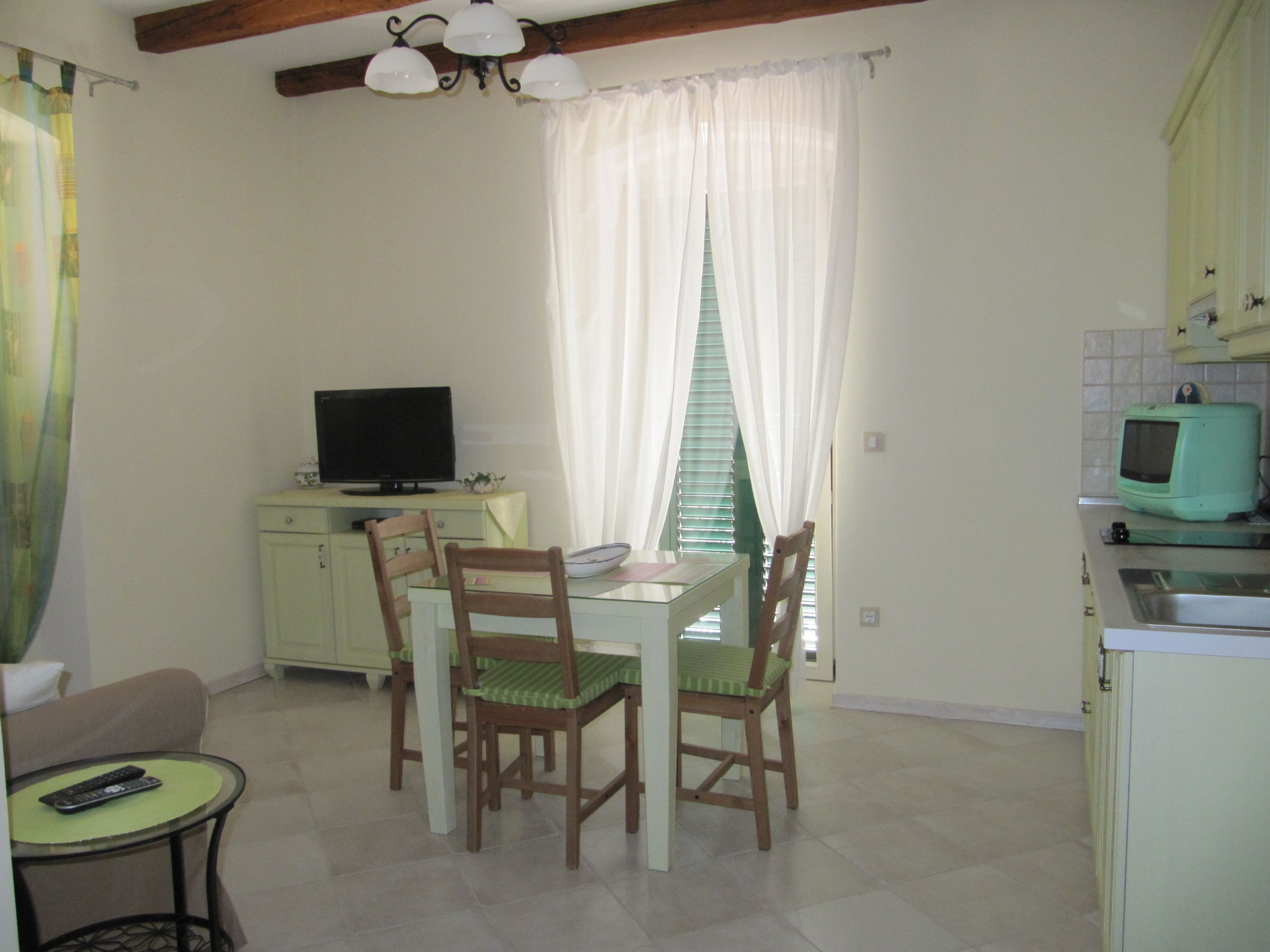 A small kitchen with a dining table, chairs, a television, and a refrigerator.