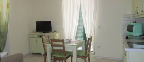 A small kitchen with a dining table, chairs, a television, and a refrigerator.