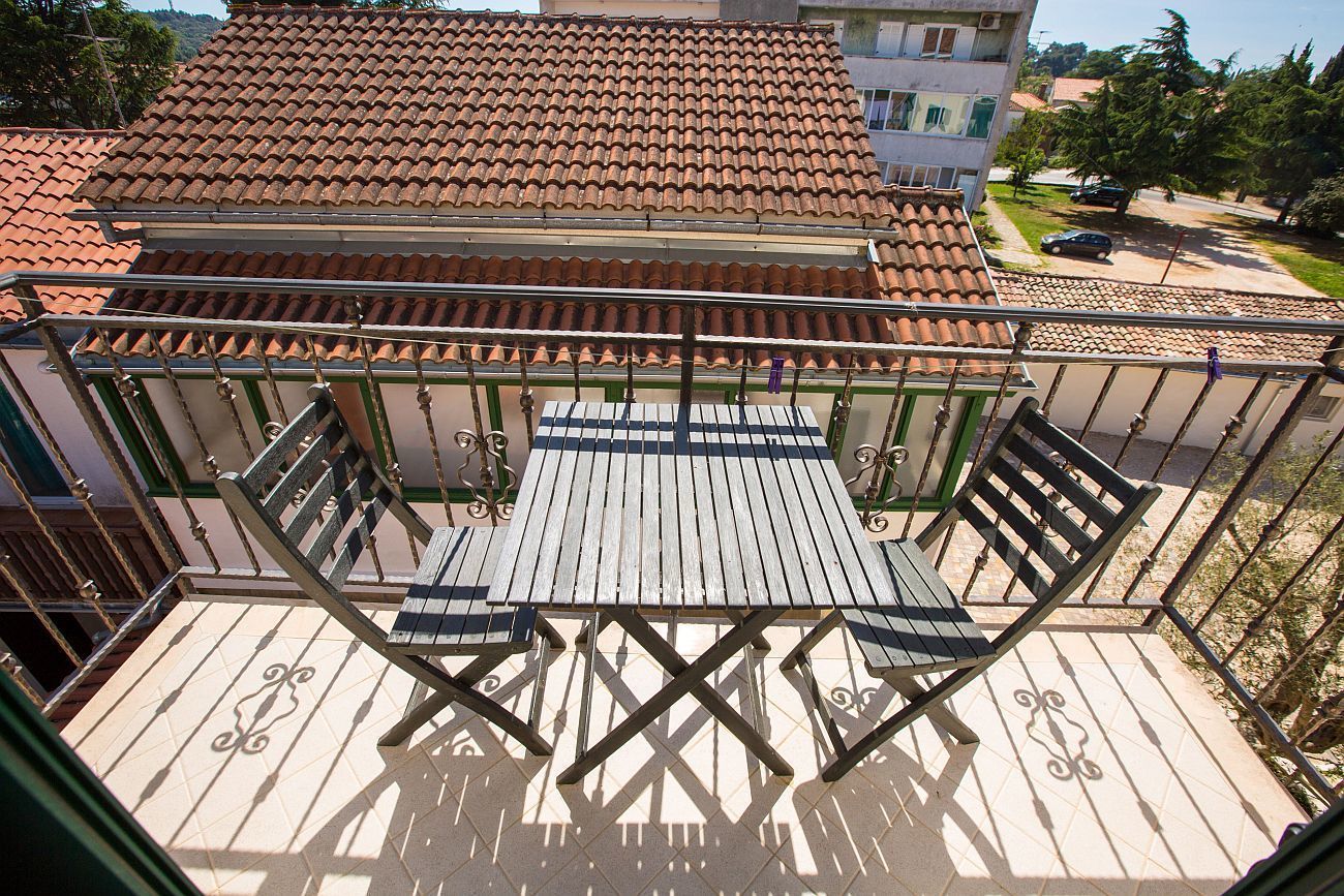 Un balcón con mesa y sillas de madera, techo de tejas y vista a una calle residencial.