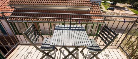 Un balcón con mesa y sillas de madera, techo de tejas y vista a una calle residencial.