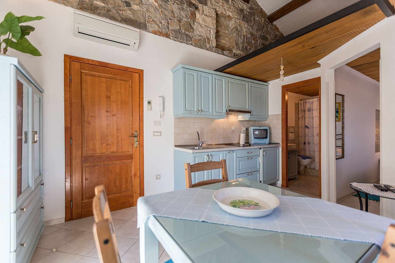 A compact kitchen with light blue cabinets, a wooden door, and a dining area with a glass table.