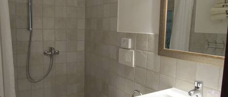 Een badkamer met douche, toilet, wastafel en spiegel.
