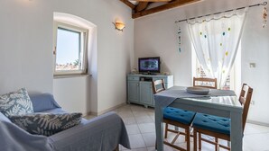 A cozy room with a sofa, a dining table with chairs, a television on a cabinet, and a window with curtains. - Apartments Casa Saina (Rovinj)