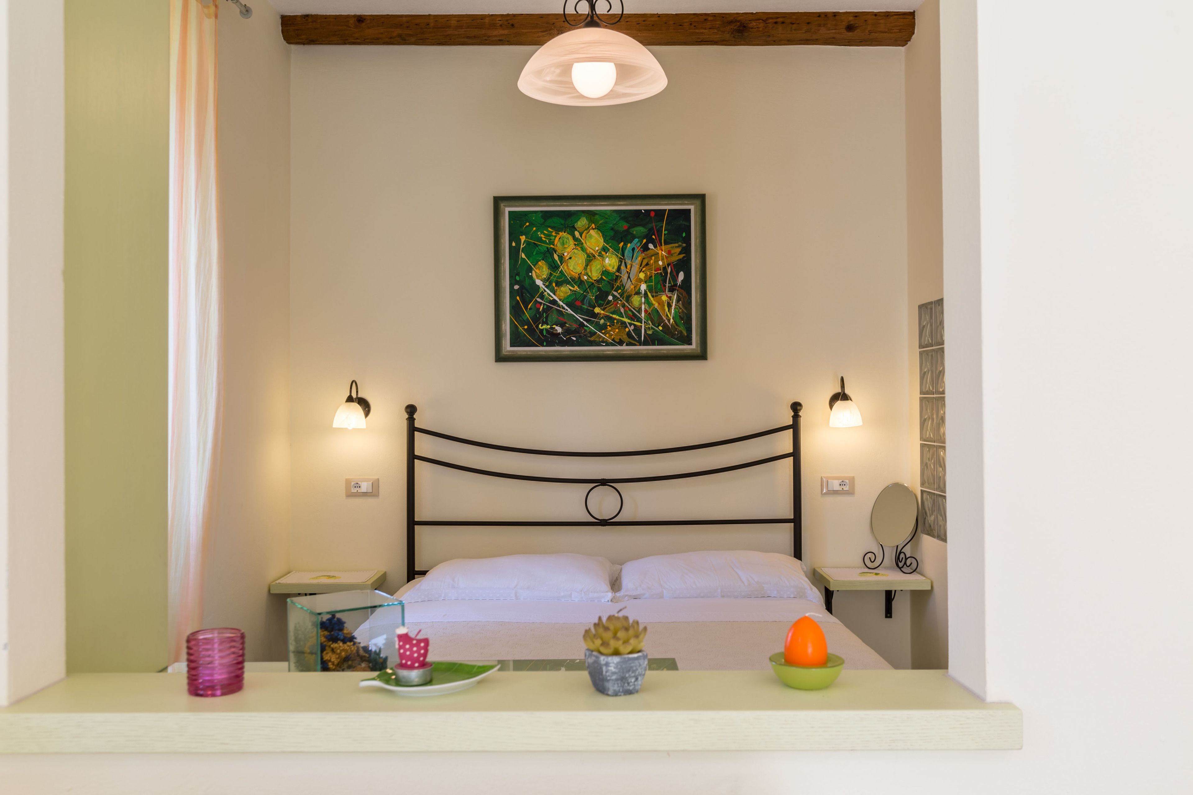 Ein Schlafzimmer mit Bett, Nachttischlampen, einem Nachttisch, einem Wandbild und einem Fenster mit Vorhang.