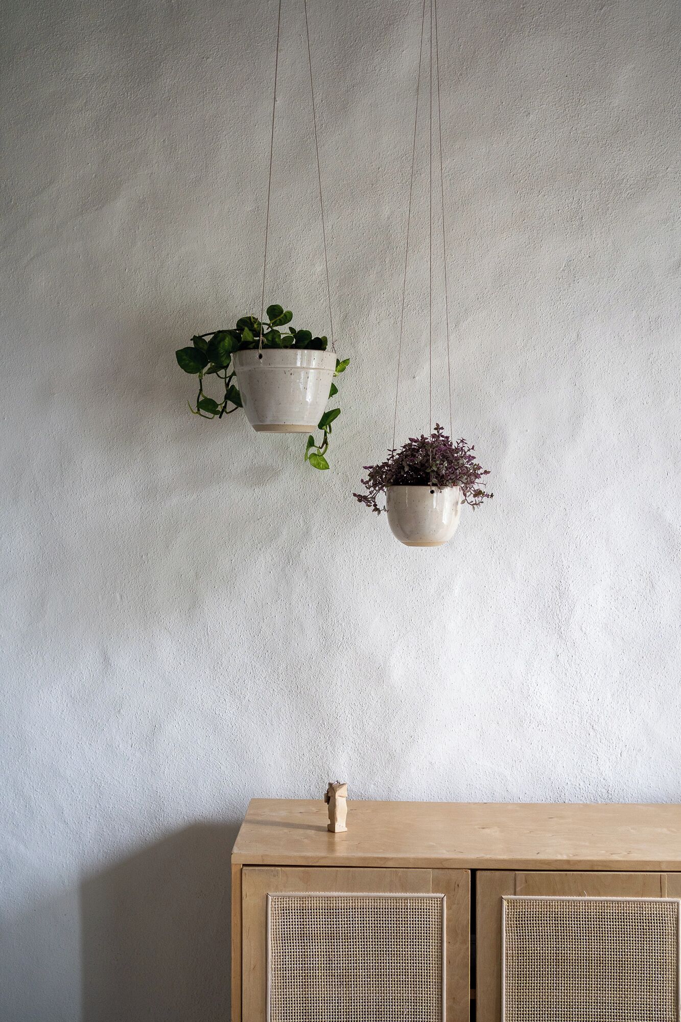 Two hanging planters with plants on a textured wall, a wooden cabinet below.