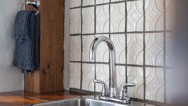 A kitchen with a stainless steel sink, wooden countertop, and a patterned backsplash. - Owl's Nest Suites (Prince Edward)