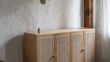 A bedroom with a wooden wardrobe, a hanging plant, and a bed with a grey blanket.