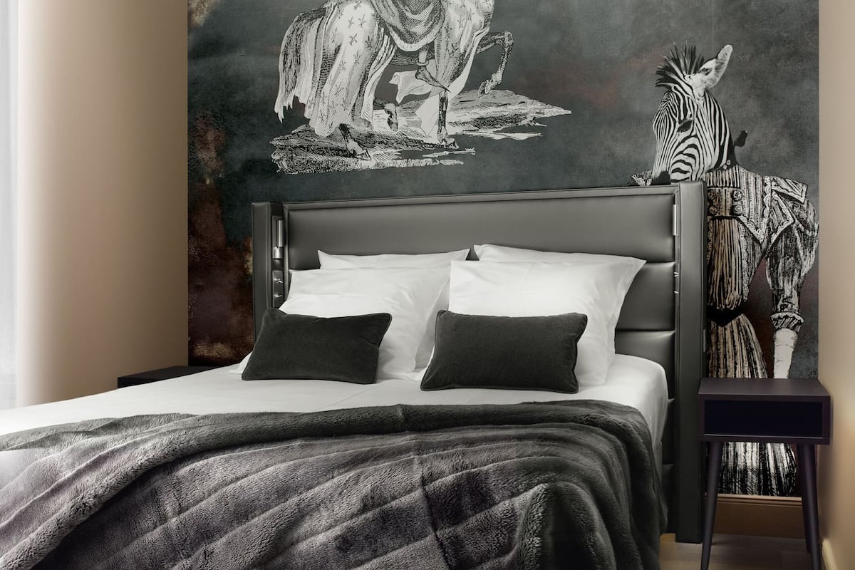 A bedroom with a bed, a headboard, a wall mural, a nightstand, and a chair.