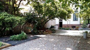 A courtyard with a gravel path, wooden furniture, and a brick wall. - Residence Le Moon (Strasbourg)