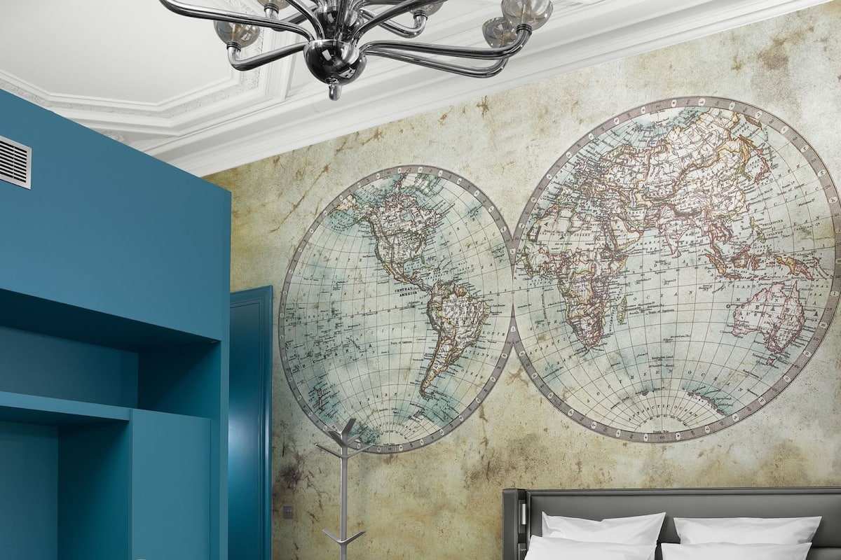 A bedroom with a large bed, two round wall maps, a chandelier, and a blue accent wall.
