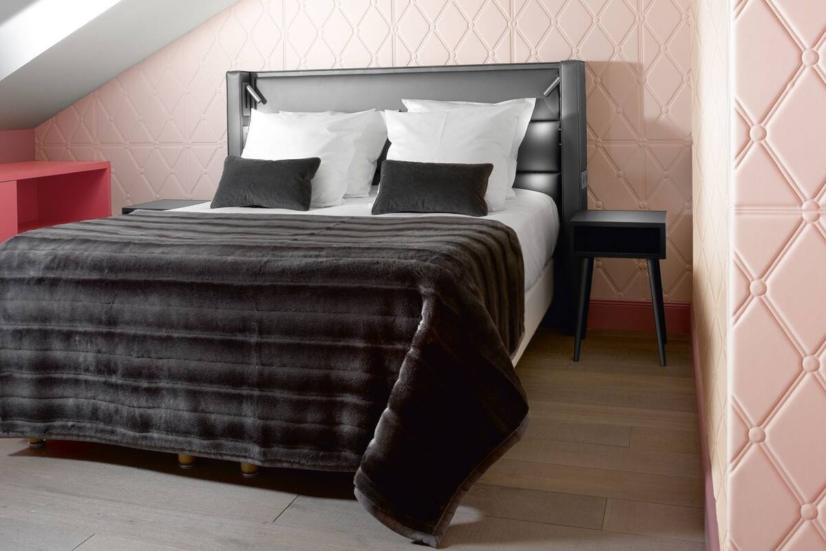 A bedroom with a sloped ceiling, a bed with a dark headboard, a nightstand, and a red side table.