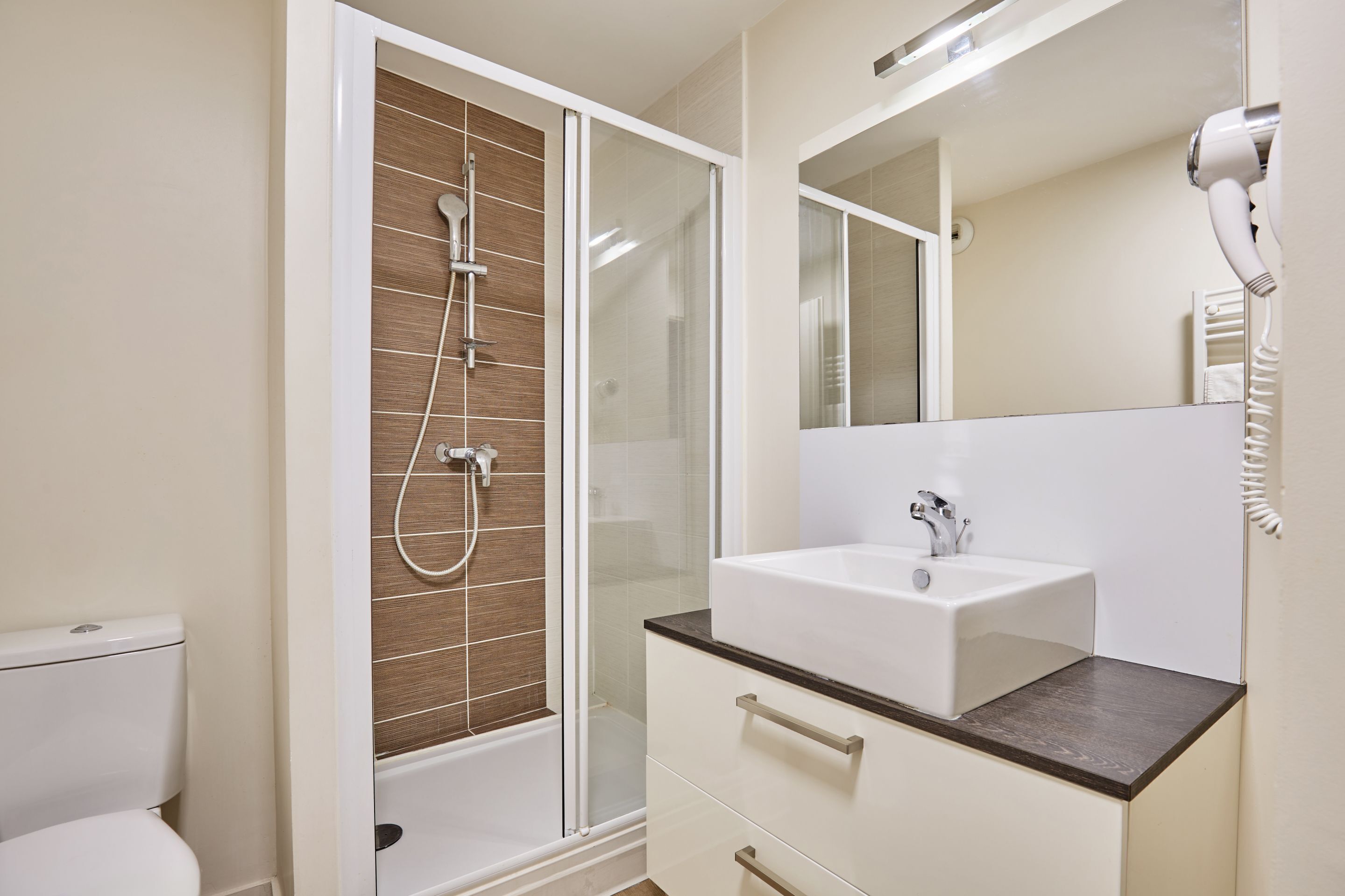 A modern bathroom with a glass-enclosed shower, a white sink, and a hairdryer on the wall.