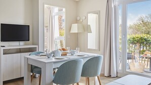 Un espace repas moderne avec une table blanche, des chaises bleues et un téléviseur posé sur un meuble blanc.