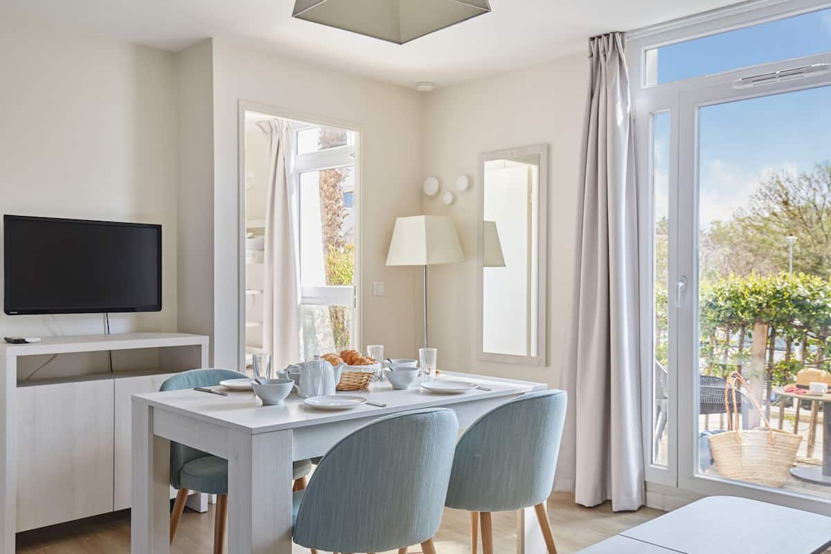 Een moderne eetruimte met een witte tafel, blauwe stoelen en een televisie op een wit kastje.