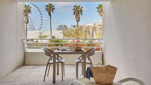 Un balcon avec une table et des chaises, un panier en osier et une vue sur une grande roue et des palmiers.