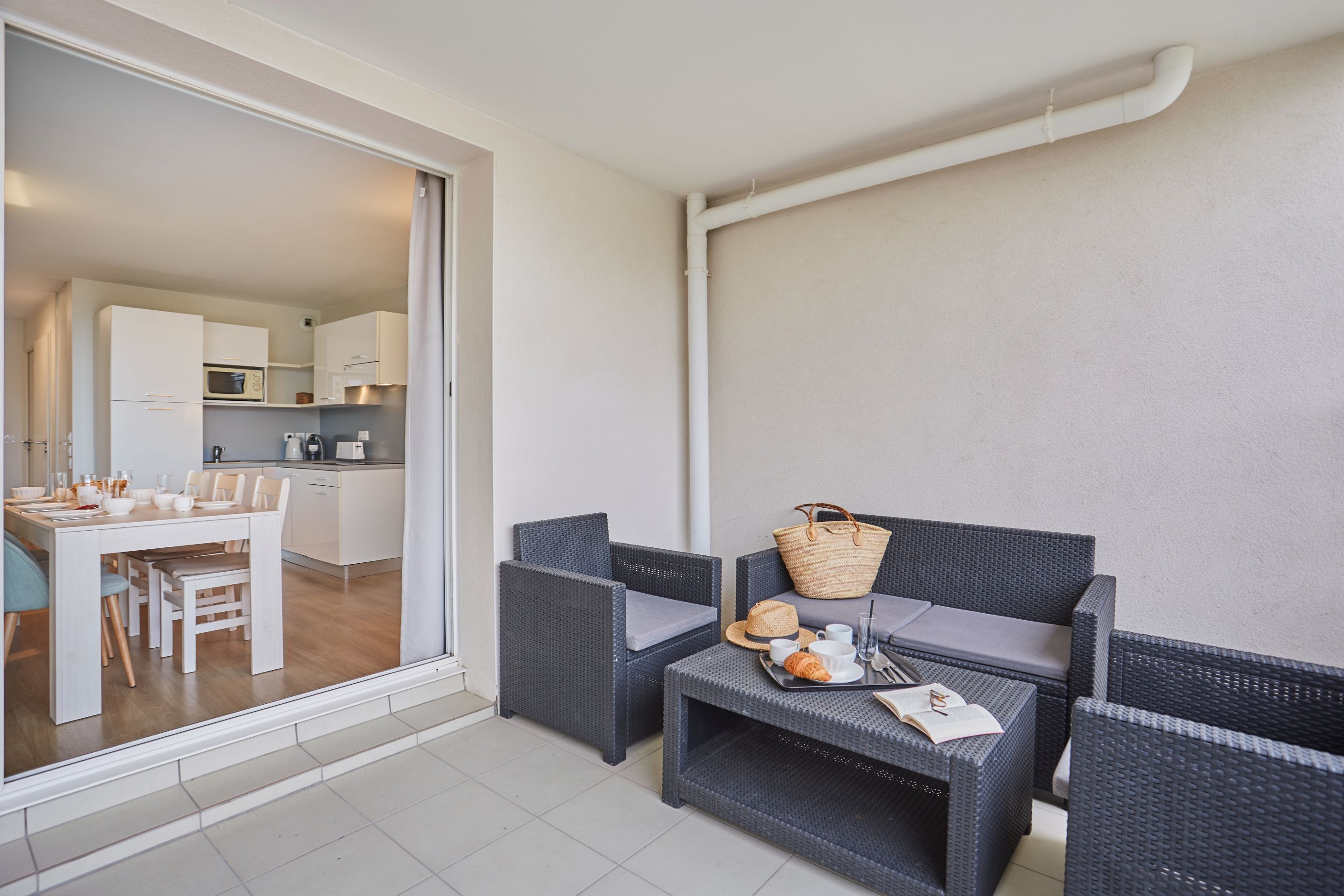 A balcony with a dining area, wicker furniture, and a kitchen visible through the glass door.