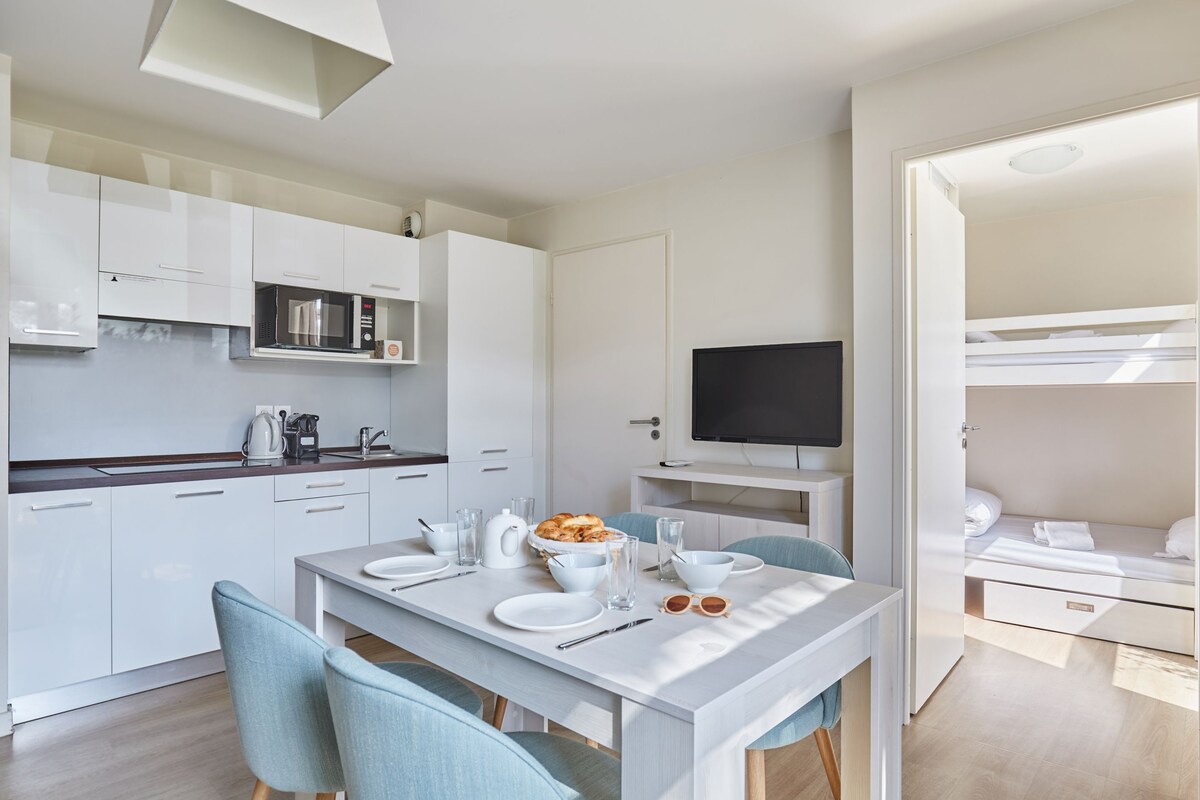 Une cuisine moderne avec des meubles blancs, un four à micro-ondes et un coin repas avec une table dressée pour deux personnes.