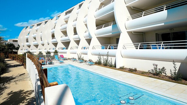 Un hôtel moderne doté d’une piscine, de nombreux balcons et offrant une vue sur un ciel d’un bleu éclatant.