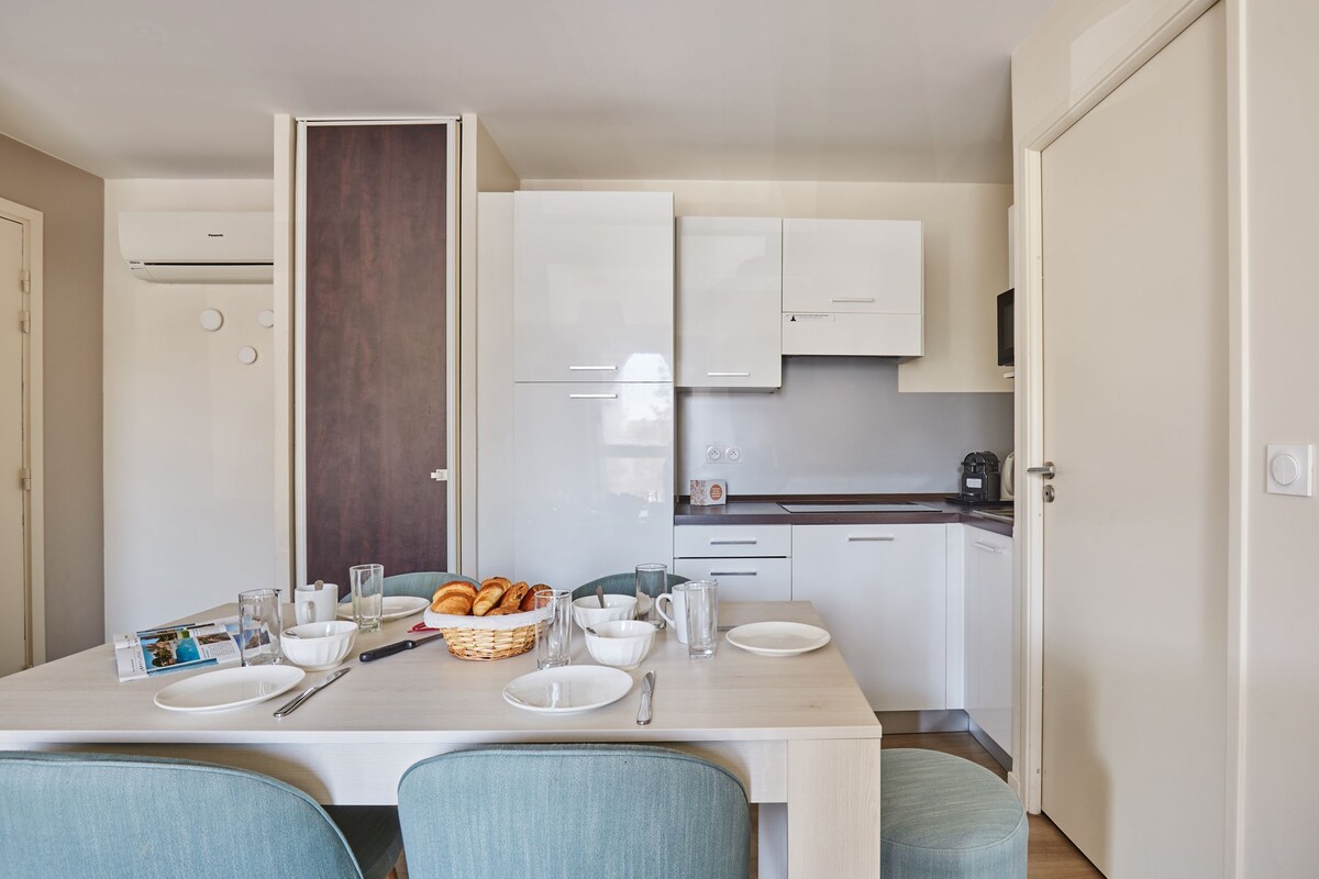 Une cuisine moderne avec des meubles blancs, une table à manger dressée avec des assiettes, des verres et un panier de pain.