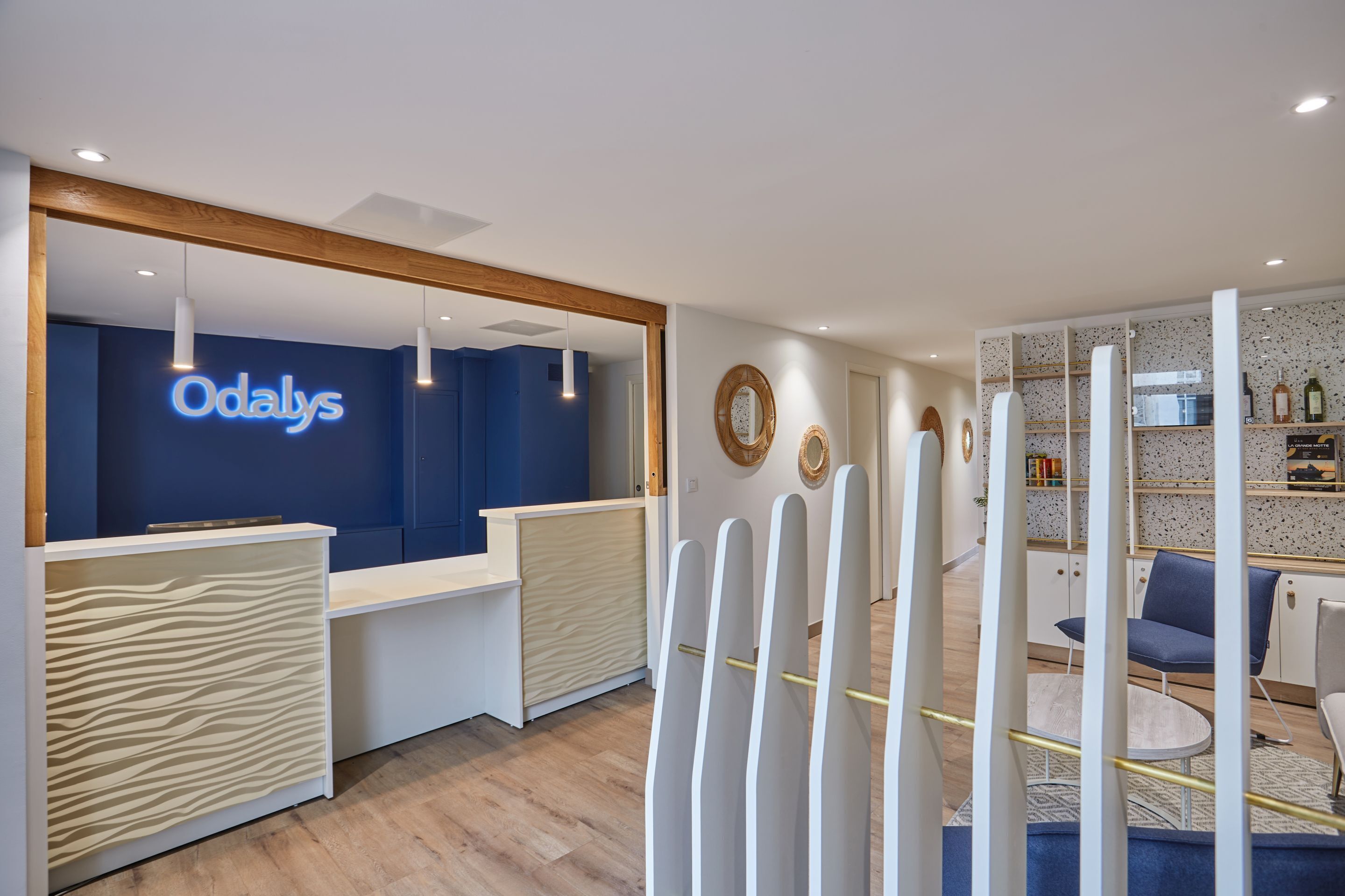 Et receptionområde med en blå væg og et neonskilt med teksten "Odalys". Der er receptionsdiske, en trædisk og et siddeområde med stole og et bord.
