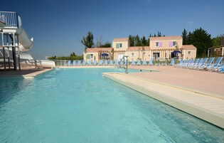 A swimming pool with a water slide, lounge chairs, and a building with a tiled roof.