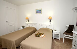 Una habitación de hotel con dos camas individuales, una mesita de noche con lámpara, una silla y un aparador.