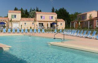Una piscina con sillas de descanso y un edificio con varias ventanas y puertas.