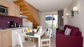 A compact living space with a kitchen, dining area, and a red sofa. - Résidence Odalys Le Mas des Alpilles (Paradou)