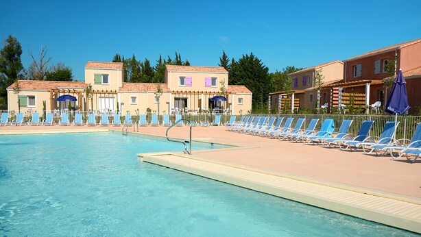 A swimming pool with lounge chairs and umbrellas, surrounded by buildings with a Mediterranean architectural style. - Résidence Odalys Le Mas des Alpilles (Paradou)