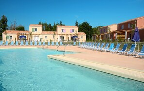 A swimming pool with lounge chairs and umbrellas, surrounded by buildings with a Mediterranean architectural style. - Résidence Odalys Le Mas des Alpilles (Paradou)