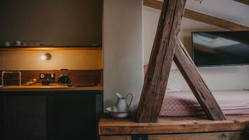 A rustic room with a wooden bed frame, a television mounted on the wall, and a wooden table with a kettle and cups.