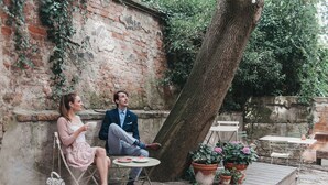 A couple sitting on a wooden deck with a brick wall and greenery in the background. - Miss Sophie's Olomouc (Olomouc)