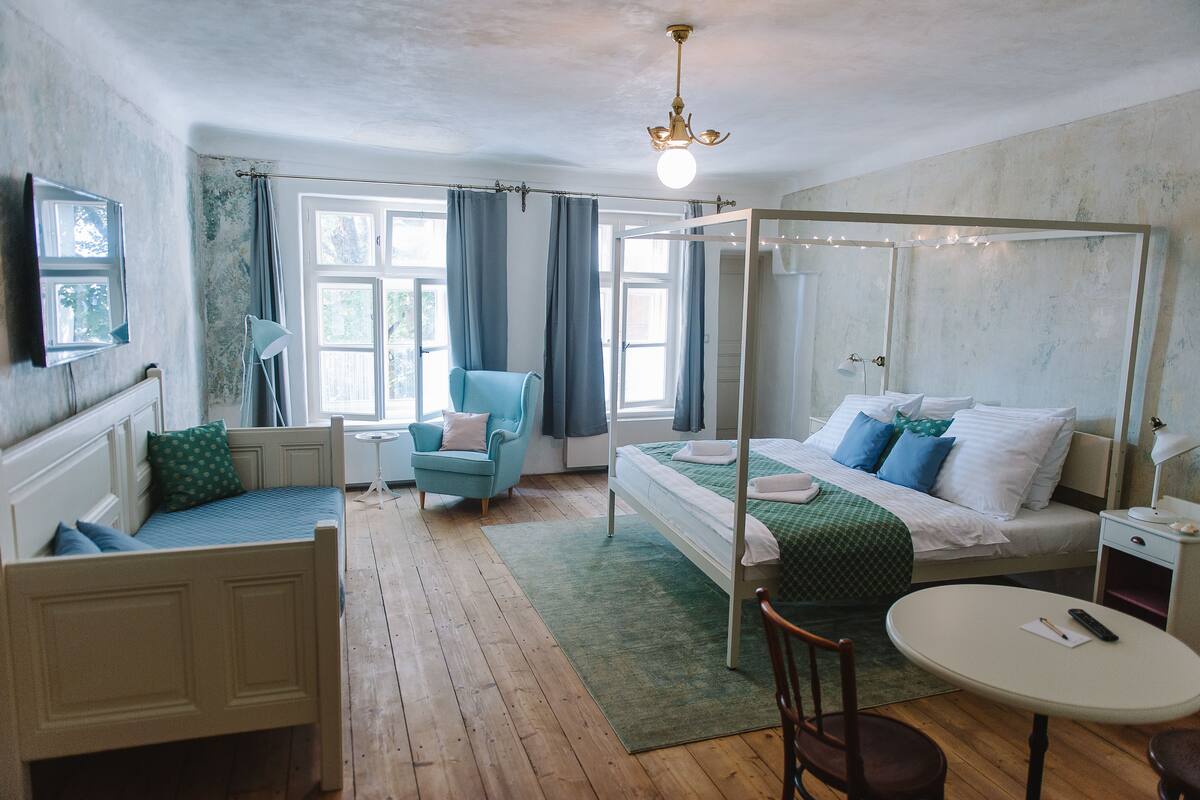 A bedroom with a four-poster bed, a single bed, a chair, a table, and a window with curtains.